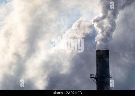 El humo blanco grueso y el vapor salen de una choza de humo en una fábrica textil industrial, llenando el cielo con nubes gruesas en un frío día de invierno. Foto de stock