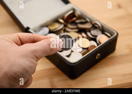 Disparo de ángulo alto de una persona que sostiene una moneda una caja llena de monedas en una superficie de madera Foto de stock