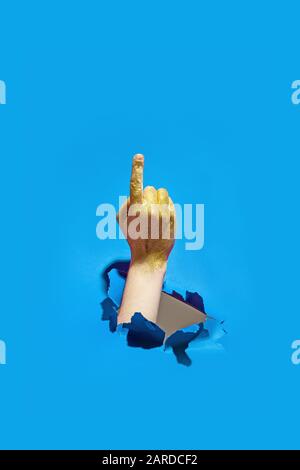Mano macho gestual con purpurpurina dorada a través de papel azul rasgado. Foto de stock