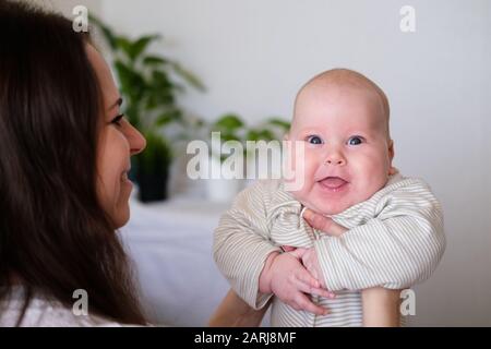 Bebé feliz. Niño blanco chubby blanco pequeño más pequeño que mira y sonríe a la cámara en las manos de la madre. La vida familiar, el amor de las madres, la maternidad