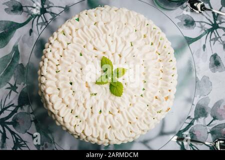 Vista superior de un pastel casero de queso de menta con glaseado blanco y hojas verdes de menta. Servido en un plato de vidrio.