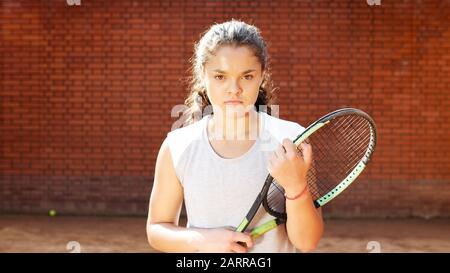 Retrato de la chica de juegos de tenis bastante joven con raqueta en pista de tenis de arcilla naranja
