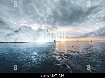Hermoso color rojo velero en el ártico junto a un enorme iceberg que muestra la escala. Navegando entre témpanos flotantes en la bahía Disko glaciar durante Foto de stock