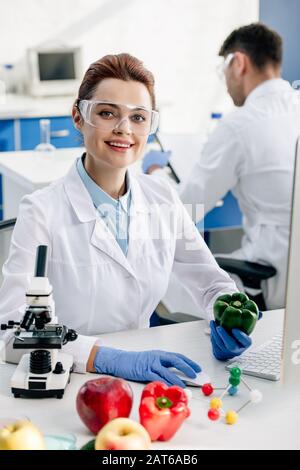 sonriente nutricionista molecular sosteniendo el pimiento y mirando a la cámara Foto de stock
