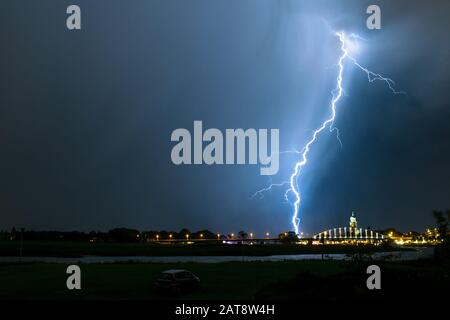 Un relámpago forked golpea abajo de una tormenta cerca de un puente en una ciudad Foto de stock