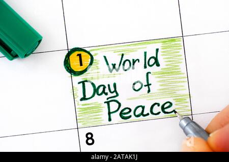 Mujer dedos con pluma verde escribir recordatorio día Mundial de la Paz en el calendario. Enero De 01. Foto de stock