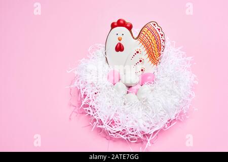 Desde arriba vista de las galletas glaseadas en forma de pollo encantador sentado en huevos coloridos en nido blanco aislado en fondo rosa. Pastel lindo. Concepto de vacaciones de primavera y semana santa. Foto de stock