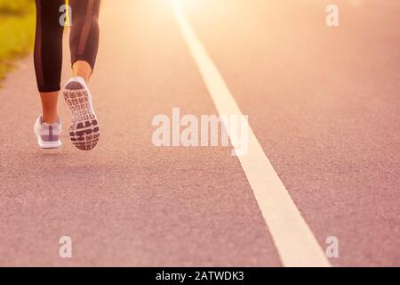Cerca de Sporty mujer corriendo en la carretera al atardecer. Concepto de bienestar de fitness y entrenamiento. Foto de stock