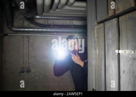 Vista trasera de un guardia de seguridad de pie en el sótano sosteniendo la linterna Foto de stock