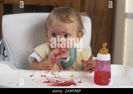 Un niño anglosajón de diez meses hace un lío comiendo moras frescas en su silla alta en casa en Austin, Texas.