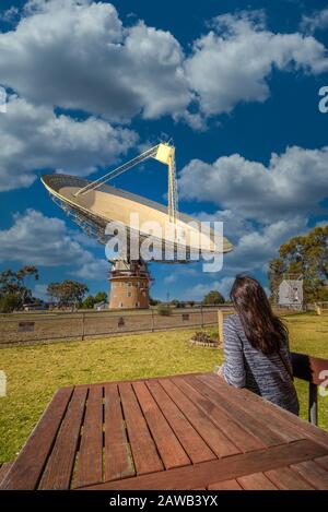 Turista femenino sentado en una mesa mirando hacia el Telescopio de Radio Parkes conocido como 'el plato' que se apunta hacia el cielo en Nueva Gales del Sur, Australia. Foto de stock