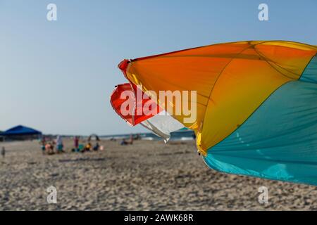 Una sombrilla de colores brillantes y azotada por el viento que se colora en un día soleado perfecto en la playa Foto de stock