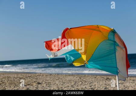 Brillante color, azotado por el viento, sombrilla rota rompiendo en un perfecto día soleado en la playa. Foto de stock