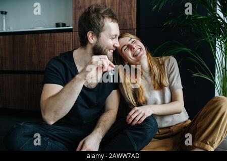Feliz pareja sentado en un piso, el hombre está sosteniendo las llaves, se han mudado Foto de stock