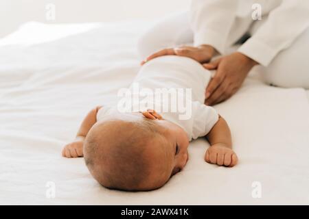 Desde arriba de mamá cariñosa con la madre recién nacida patting bebé pequeño asiático acostado en la barriga en el dormitorio en casa Foto de stock