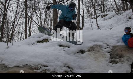 Snowboarder salta del acantilado de hielo en el bosque Foto de stock