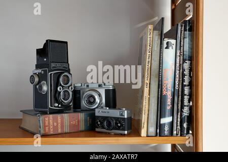 Una fotografía de tres cámaras y libros de fotografía vintage colocados en un estante.