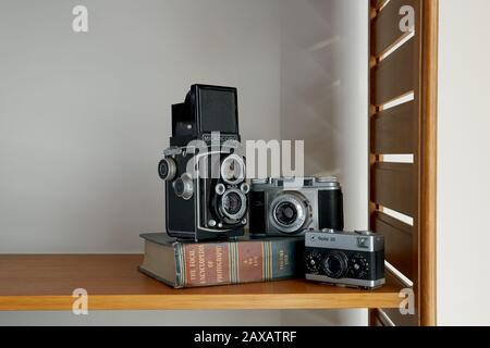 Una fotografía de tres cámaras vintage y un libro de fotografía vintage colocado en un estante.