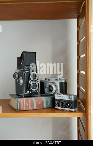 Una fotografía de tres cámaras vintage y un libro de fotografía vintage colocado en un estante.