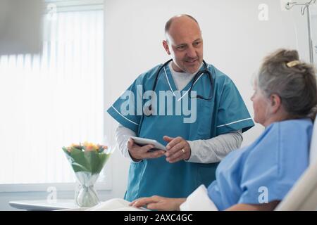 Médico con tabletas digitales haciendo rondas, hablando con el paciente mayor en la sala del hospital Foto de stock
