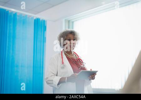 Médico senior femenino con tabletas digitales realizando rondas en la sala del hospital Foto de stock