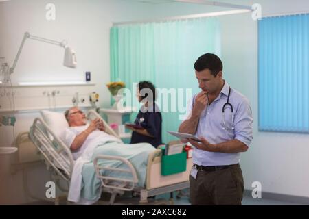 Médico masculino con tableta digital haciendo rondas en la sala del hospital Foto de stock