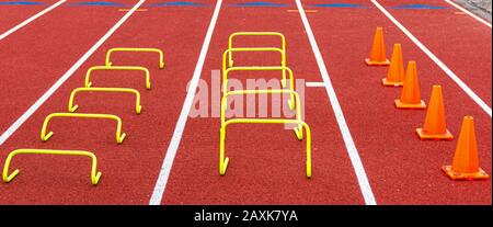 Mini bannana amarilla con vallas y conos de naranja en carriles en una pista roja para ejercicios de práctica de velocidad y agilidad.