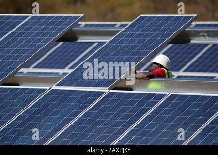 Trabajadores que instalan una matriz de paneles solares en un campo abierto en el sur de Vermont Foto de stock