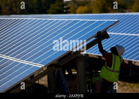 Trabajadores que instalan una matriz de paneles solares en un campo abierto en el sur de Vermont Foto de stock
