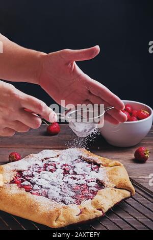 Manos de la mujer rociando pastel de fresa recién horneado Foto de stock