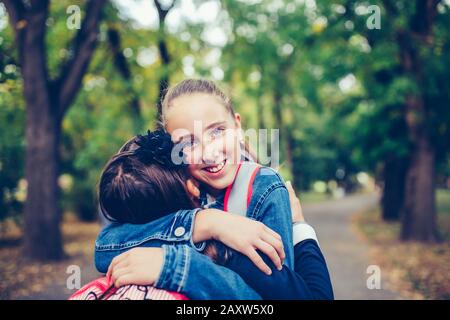 Dos amigos de la escuela abrazando, reunión emocional en el parque. El concepto de escuela, estudio, educación, amistad, niñez Foto de stock