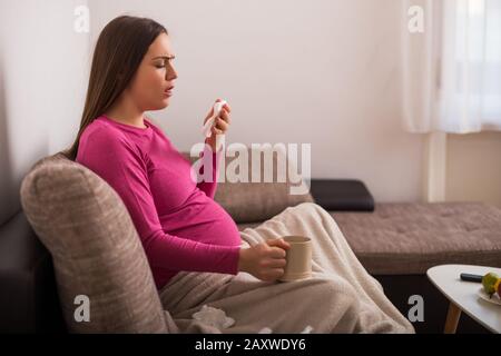 Exhausta mujer embarazada tosiendo mientras toma gripe y té. Foto de stock