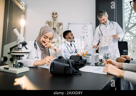 Hermoso profesor masculino con estudiantes de medicina multiétnica o científicos que usan batas de laboratorio en el salón de clase. Joven y bonita niña musulmana es feliz y sonriente