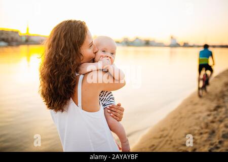 Feliz familia en la playa. Hijo niño madre niño y bebé que se acerca a la playa cerca del río o el lago. Feliz familia en la playa. Mamá y.