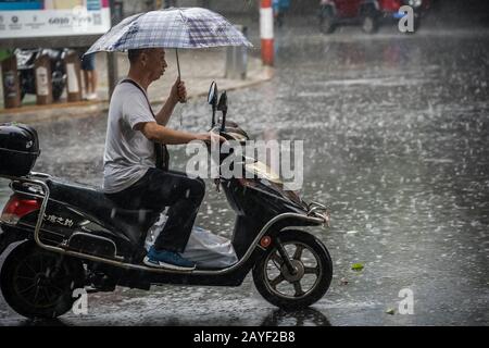 Hombre en scooter con lluvia monzónica tropical Foto de stock