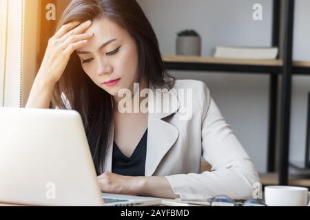 Mujer asiática joven de estrés en el trabajo, mujer deprimida en la oficina. Retrato de hermosa joven Asia mujer sintiéndose enferma, teniendo dolor de cabeza, sindrom de oficina