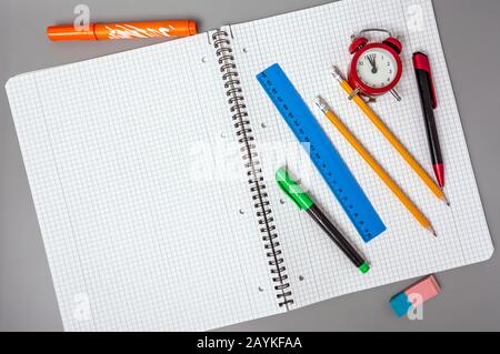 Lápices, un bolígrafo y una regla se encuentran en un cuaderno abierto. Un reloj despertador recuerda la hora. Oficina. Materiales escolares. Foto de stock