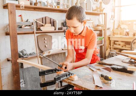 Pequeño niño genio talentoso trabaja con madera en un taller de carpintería. El concepto de aprendizaje, aficiones y trabajo manual para niños