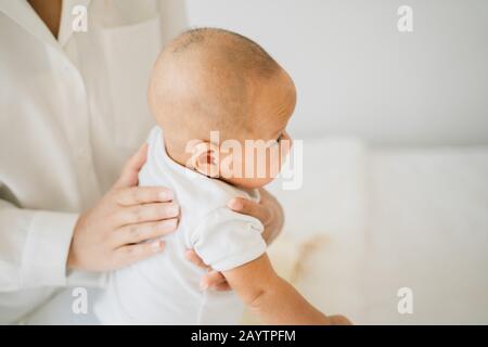 Desde arriba de la mamá acariciando a un adorable hijo recién nacido masajeando la espalda del bebé asiático en la cama en casa