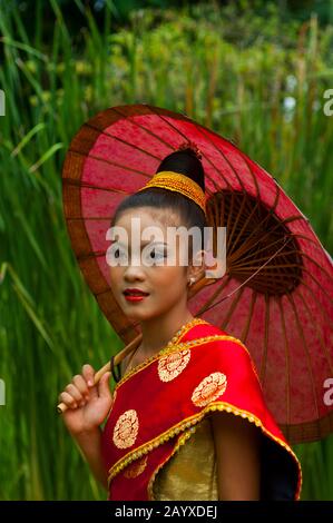 Una adolescente laosiana (VERSIÓN MODELO 2006-10-04) en un traje festivo tradicional De Las Tierras Bajas con sombrilla en el jardín de la Residence Phou Vao Hot Foto de stock