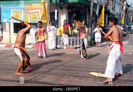 Tailandia: Devotos entranzos o "una canción" toman parte en la automutilación en una esquina de la calle durante una procesión por la ciudad de Phuket, Festival Vegetariano de Phuket. El Festival Vegetariano es un festival religioso que se celebra anualmente en la isla de Phuket en el sur de Tailandia. Atrae a multitudes de espectadores debido a muchos de los rituales religiosos inusuales que se realizan. Muchos devotos religiosos se saltan con espadas, perforan sus mejillas con objetos afilados y cometen otros actos dolorosos. Foto de stock