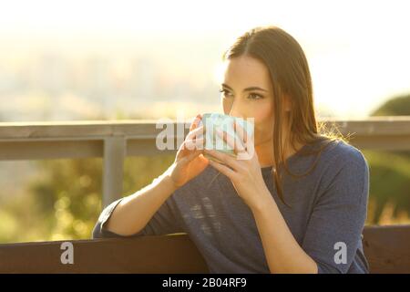 Mujer relajada bebiendo café sentado en un banco en un parque al atardecer
