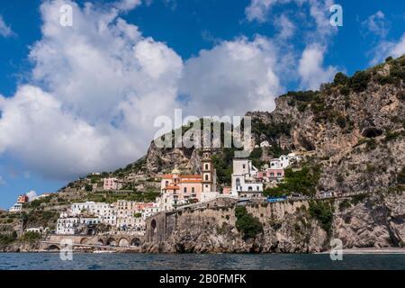 El pueblo de Atrani y la Colegiata de Santa Maria Maddalena visto desde el agua, las montañas y el cielo en el fondo, en la costa de Amalfi de Italia Foto de stock
