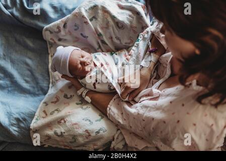 Vista superior de la madre que sostiene al recién nacido con sombrero en la cama del hospital