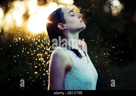 Mujer joven refrescante a sí misma en la lluvia Foto de stock