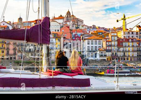 Mujeres en un yate privado beber vino y disfrutar de la vista de la puesta de sol en Porto, Portugal. Vista trasera. Panorama de la ciudad vieja de Oporto en el río Duoro. Oporto panorama