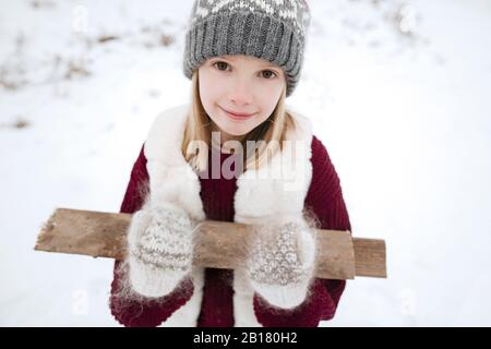Retrato de una niña sonriente que lleva leña en invierno Foto de stock