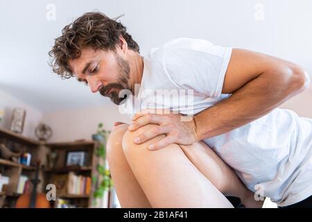 Un terapeuta profesional de masseur de mediana edad que da masaje de piernas a un hombre fuerte. Sportsman recibiendo un masaje relajante en el ambiente acogedor del hogar Foto de stock