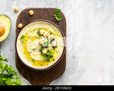 Hummus de aguacate saludable en un cuenco de cerámica con aceite de oliva, garbanzos y perejil verde picado, vista superior, espacio de copia, fondo gris.