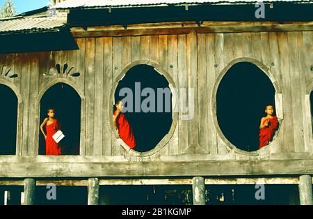 Tres jóvenes monjes novatos con túnicas rojas enmarcadas en las ventanas ovaladas del monasterio de Shwe Yan Bye, cerca de Nyaung Shwe, Lago Inle, Myanmar. Foto de stock